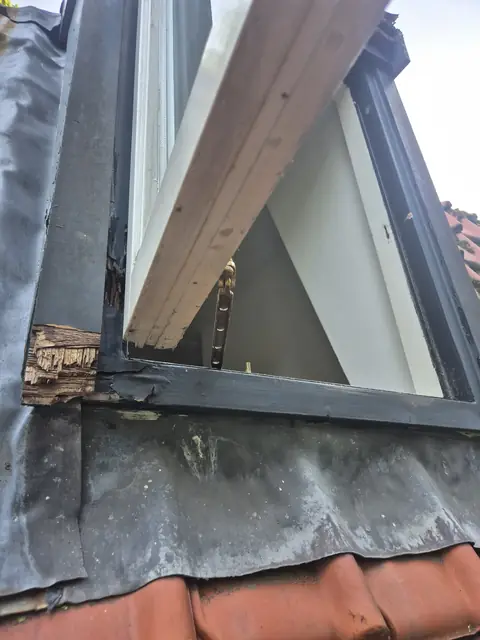Een openstaand dakraam met weggerot hout onderin het kozijn, naast het loodwerk