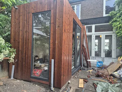 Aanbouw met verticale houten gevelbekleding, een hoog vast raam en een schuifpui naar de tuin