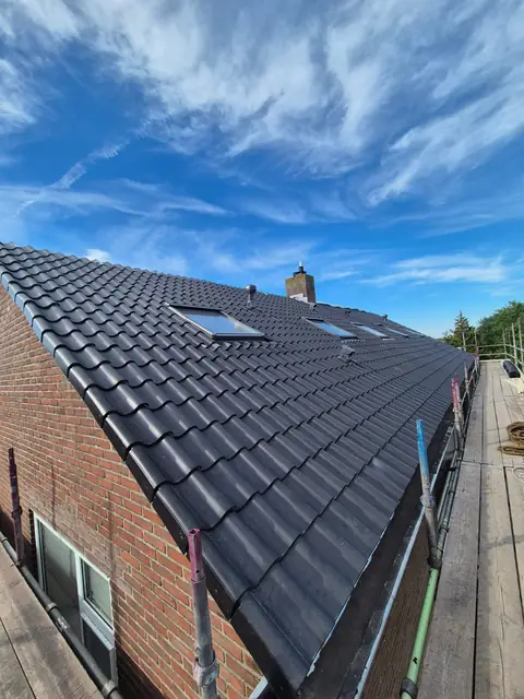 Het vernieuwde dakvlak met dakramen en schoorsteen onder een wolkenlucht