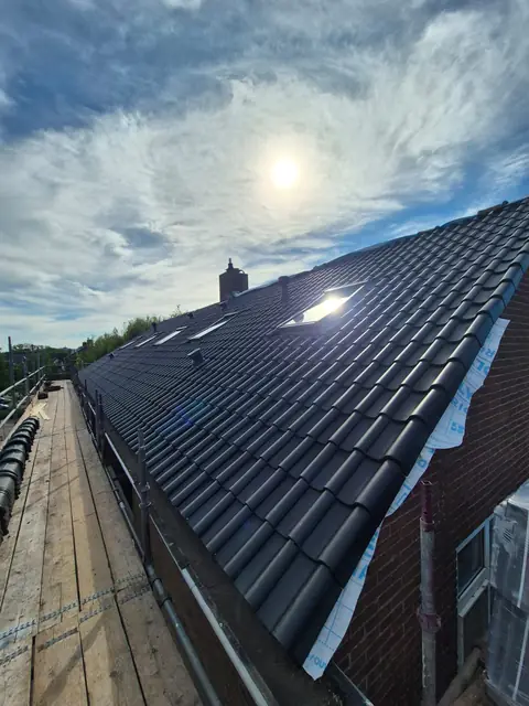 Het nieuwe pannendak in tegenlicht, met folie die nog langs de gevel hangt