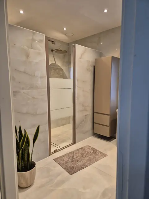 De afgewerkte badkamer met een glazen douchewand in een messing profiel, en een lage wandkast