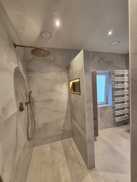 De douche van binnenuit, met de verlichte nis, de thermostaatkraan en de designradiator bij het raam